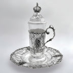 Silver teacup with lid and decorative elements on a white background