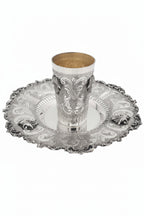 Silver kiddush cup with gold interior on an ornate silver tray against a white background