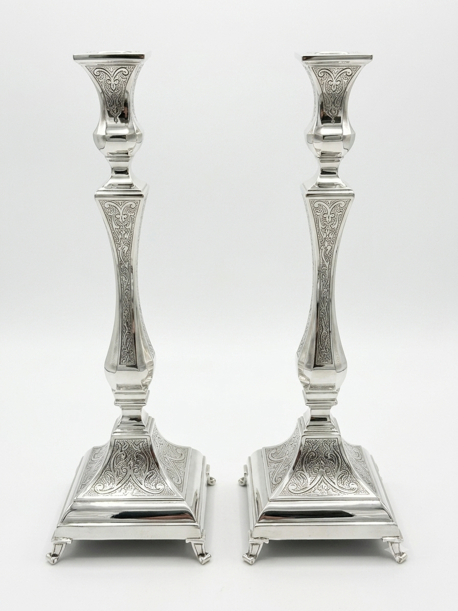 Pair of silver candlesticks with intricate engravings on a white background
