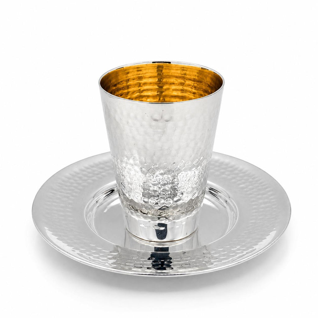 A silver hammered kiddush cup with a gold interior, shown on a matching silver hammered plate by hadad bros silverware