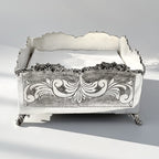 Decorative silver napkin holder box with intricate designs on a light gray background